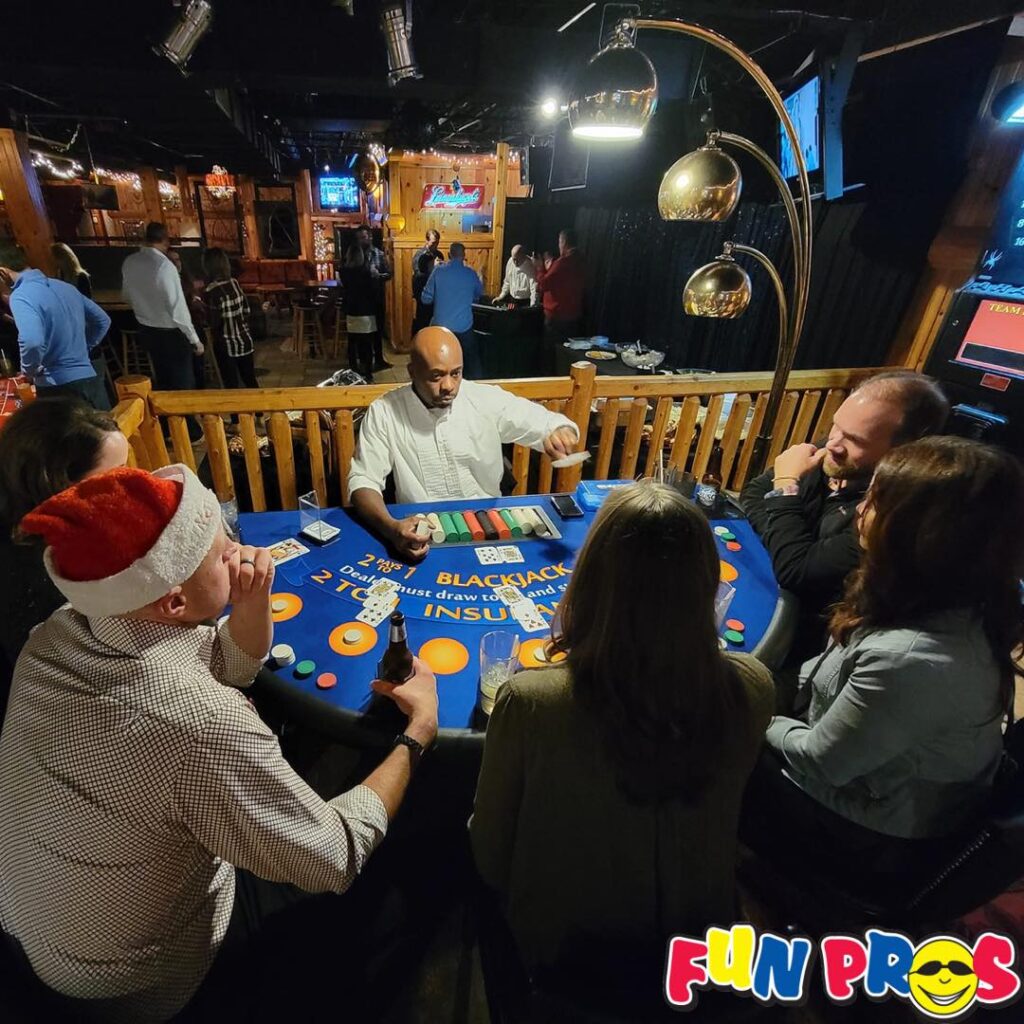 Five people play blackjack at a blue felt table with a dealer in a festive, dimly lit venue. One player wears a Santa hat. The "FUN PROS" logo is in the bottom right corner.