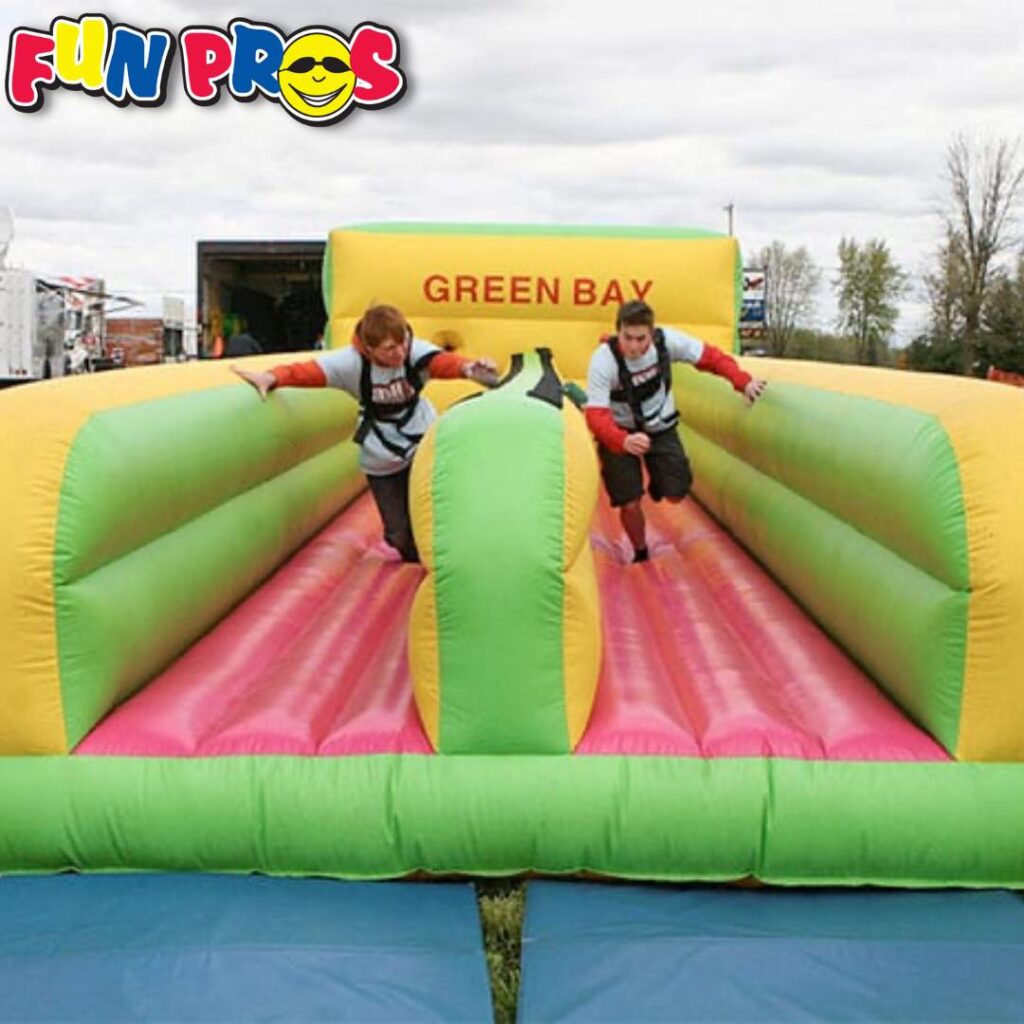 Two people in harnesses run on an inflatable bungee run game labeled "Green Bay," with the Fun Pros logo in the corner.